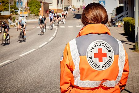 Ehrenamtliche des DRK steht an der Rennstrecke und beobachtet die Fahrradfahrer des Radrennens.