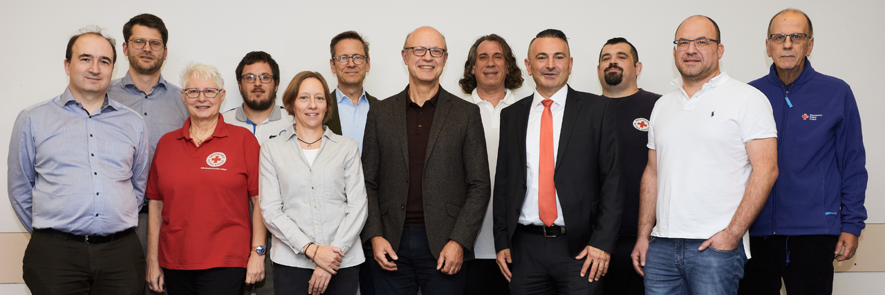 12 Personen des Kreisvorstandes des DRK Main-Taunus e.V. stehen gemeinsam lächelnd vor einer weißen Wand.