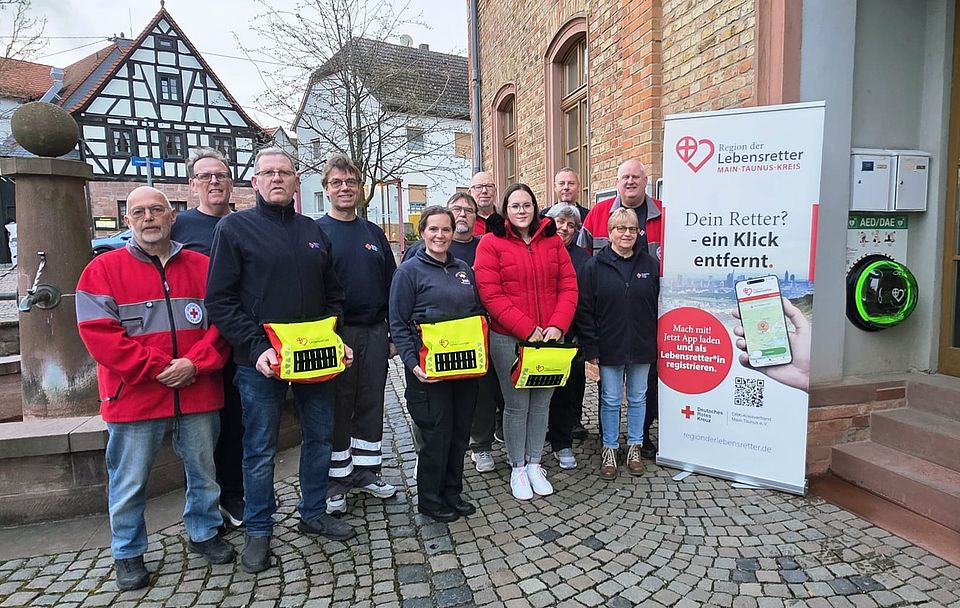 Ehrenamtliche des DRK OV Diedenbergen stehen neben des neu eingeweihten Defibrillators auf dem Platz in der Dorfmitte