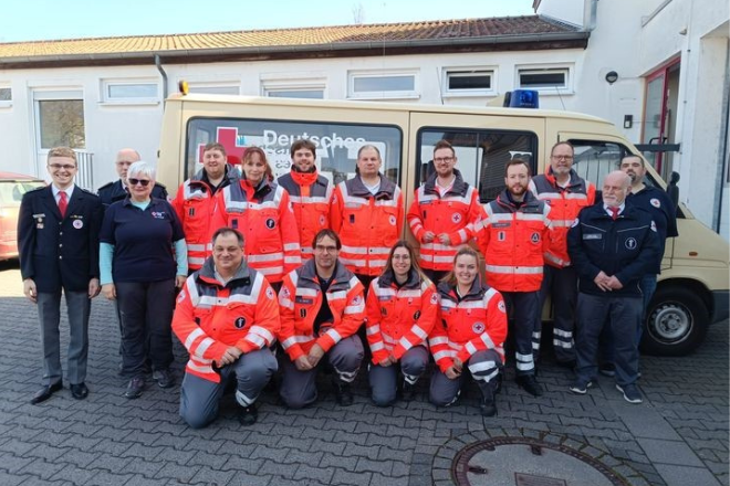 Gruppenbild der Absolventen vor einem beigen Auto des Deutschen Roten Kreuzes